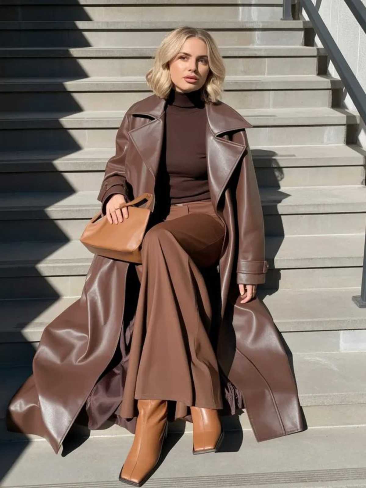 Woman in brown trench and boots sitting on steps wearing Murps outerwear.