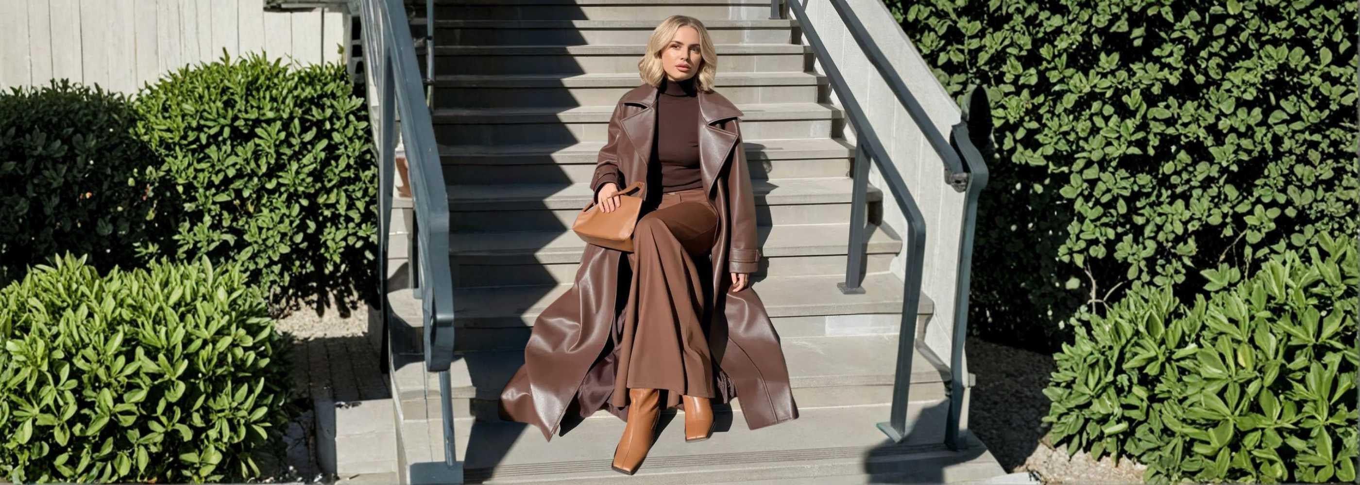 Woman in brown trench and boots sitting on steps wearing Murps outerwear.