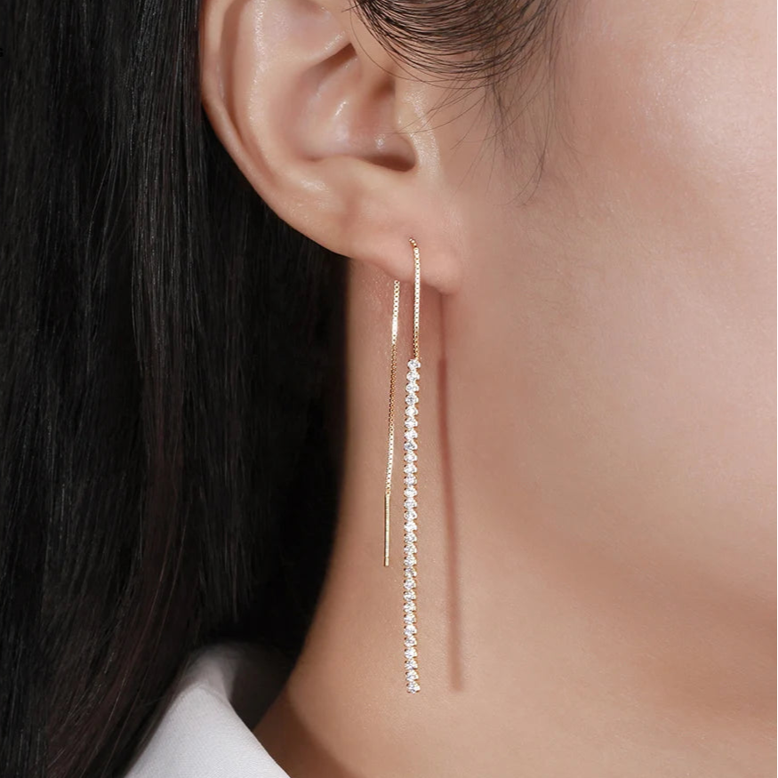 Earring worn by a person with long dark hair, close-up on a neutral background